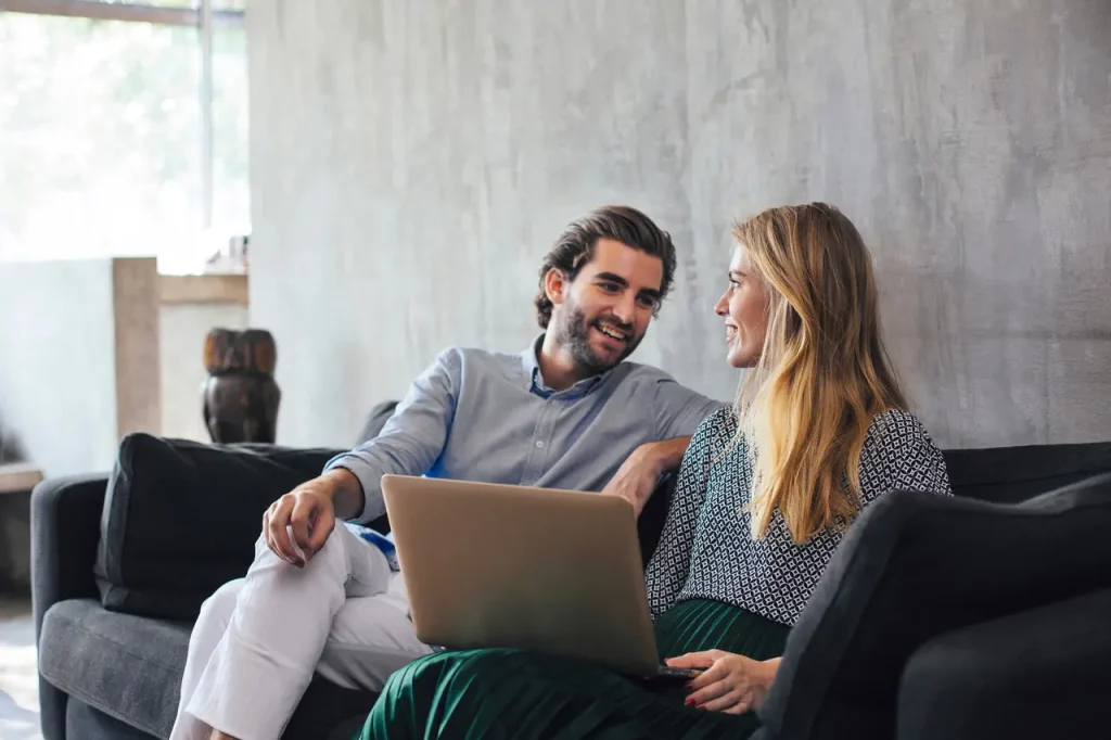 a man and woman sitting on a couch looking at a laptop