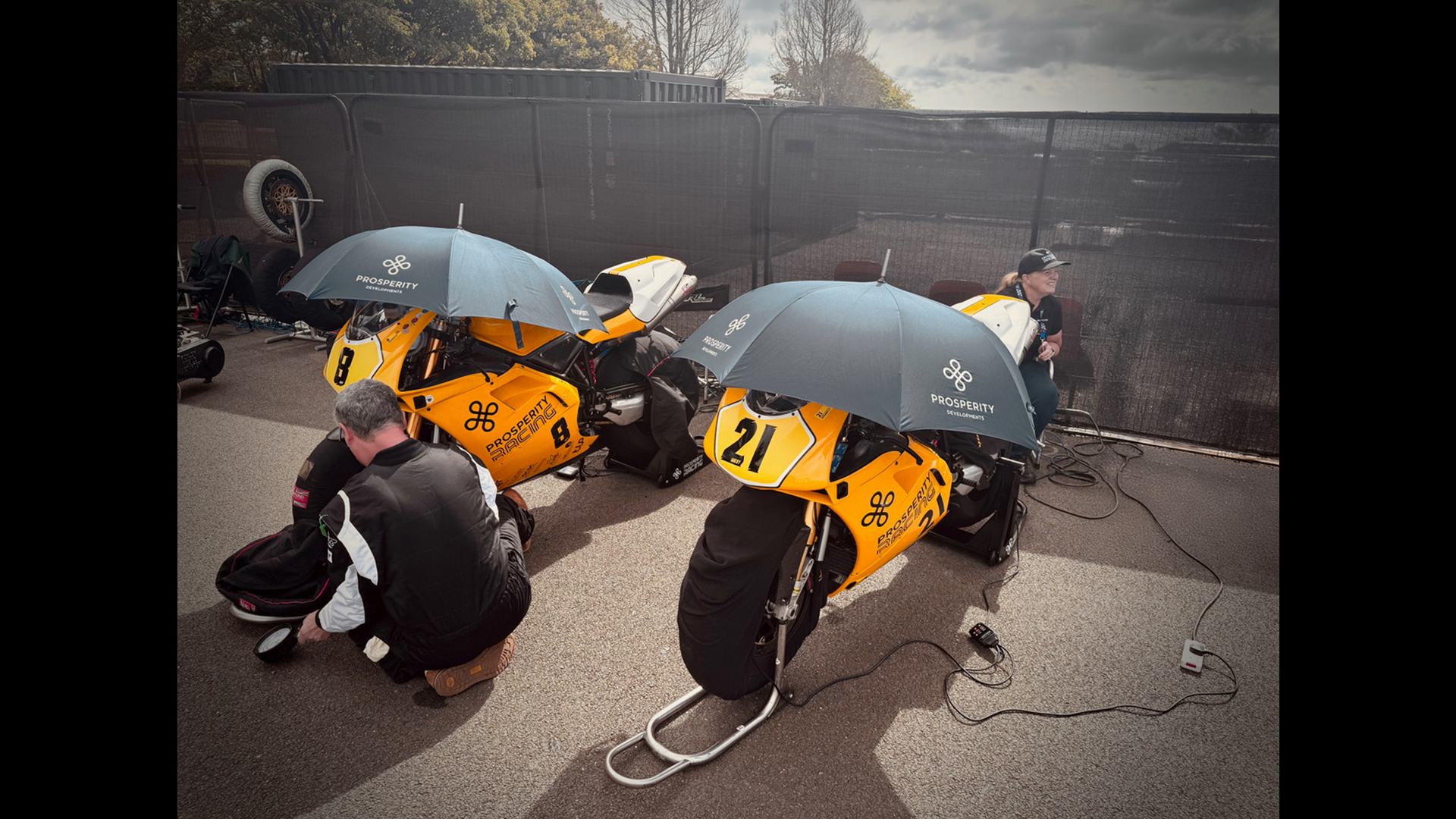 Two yellow motorbikes with umbrellas open on top featuring the Prosperity Wealth Logo