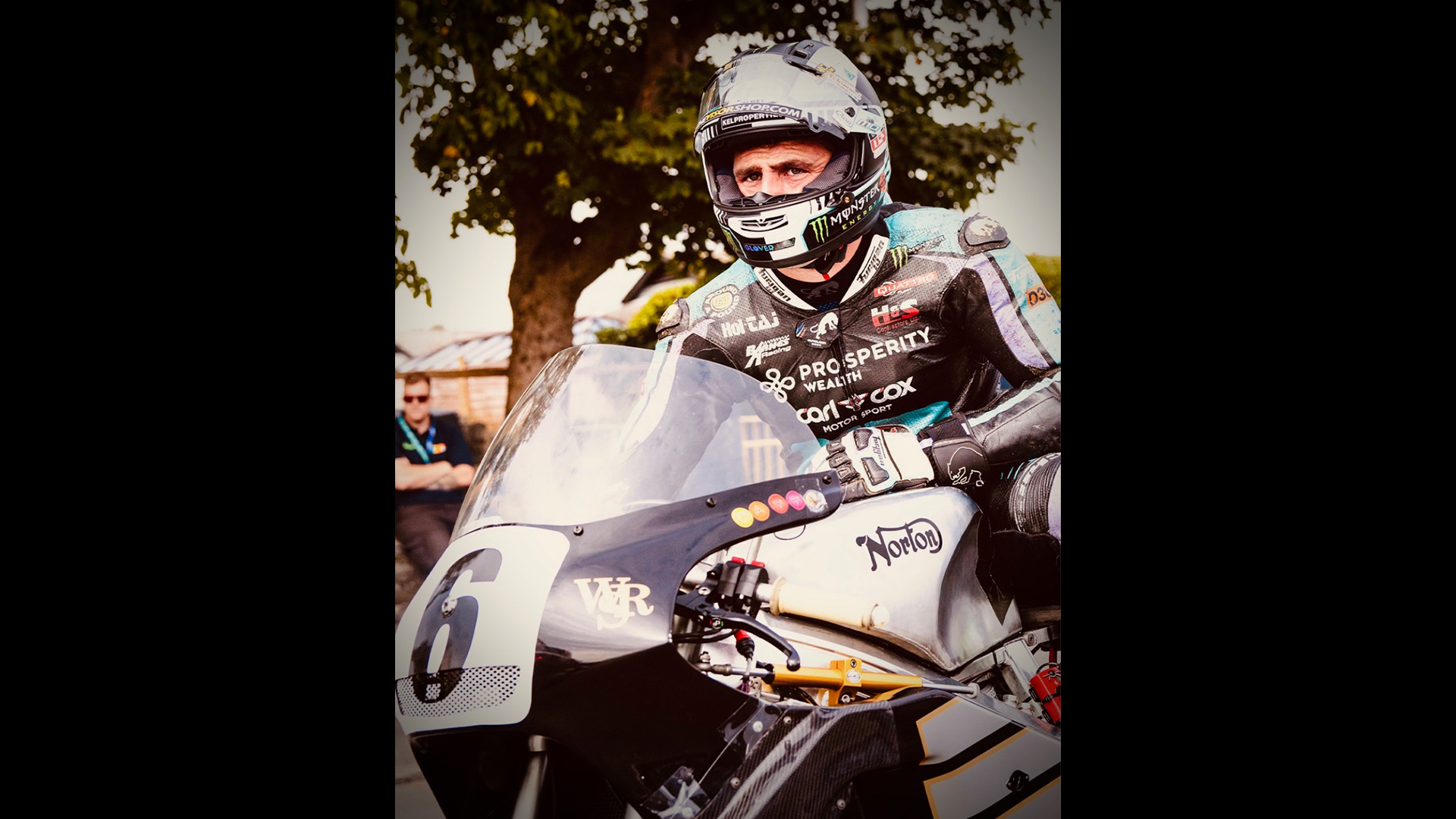 Black and silver motorbike with rider wearing helmet and a bike jacket featuring the Prosperity Wealth logo